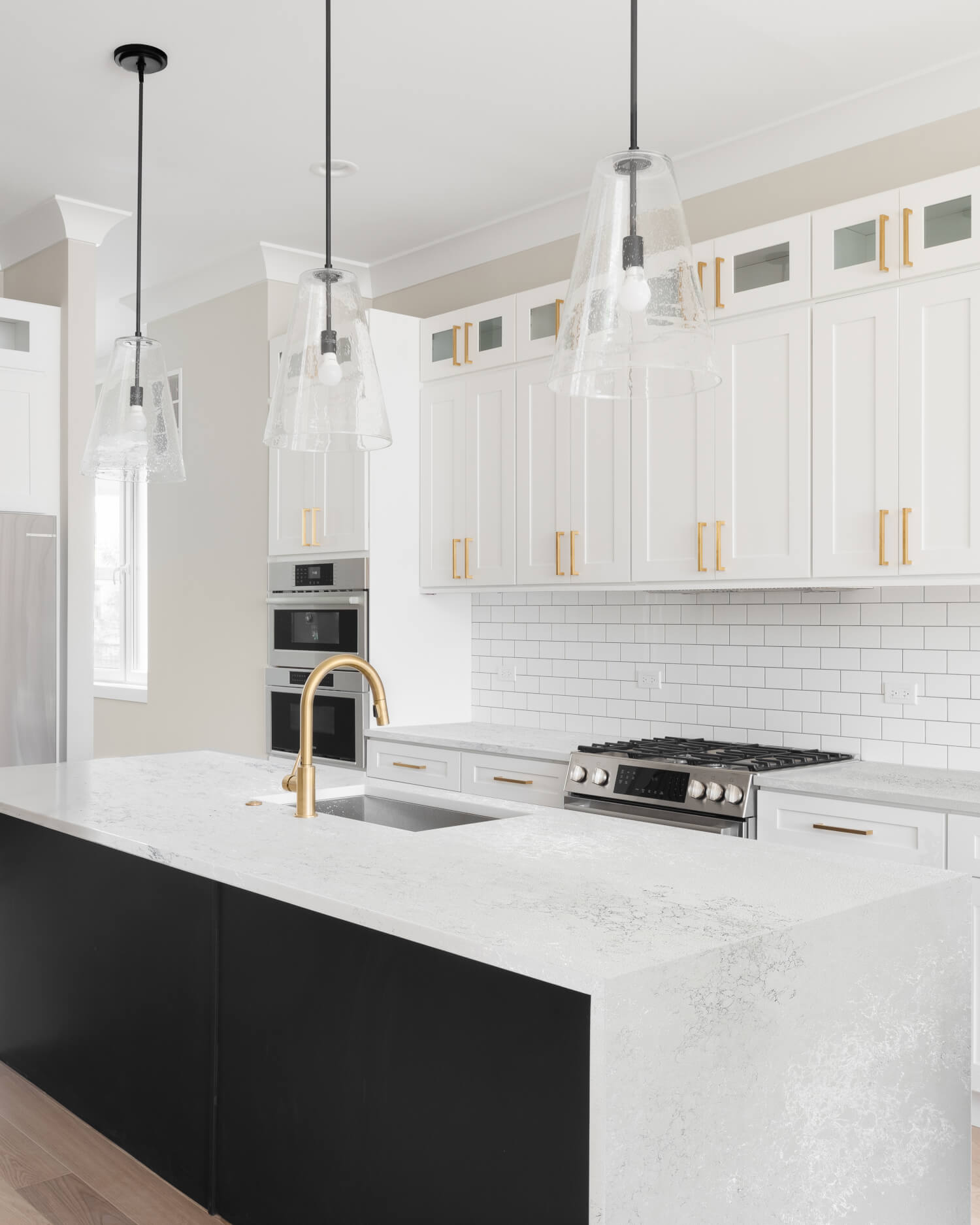 Modern kitchen with white countertops, gold fixtures, and stainless steel appliances.